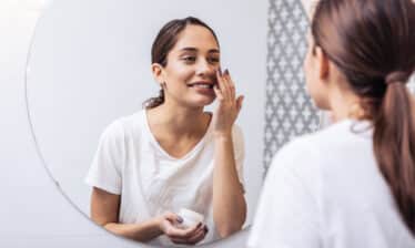 woman applying facial product in mirror